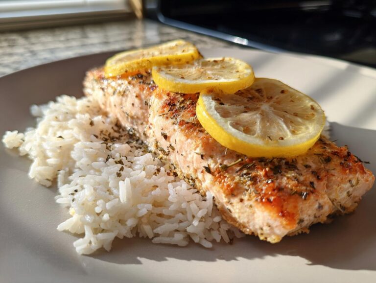 A close-up of a perfectly cooked oven baked salmon fillet served with white rice and topped with lemon slices.