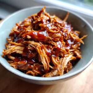 Close-up of a bowl filled with tender Instant Pot pulled BBQ chicken, glistening with sauce.