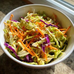Close-up of a white bowl filled with vibrant, crunchy cabbage salad featuring shredded green cabbage, purple cabbage, and carrots.