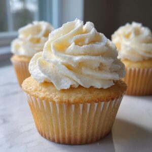 A close-up of a moist vanilla cupcake topped with a generous swirl of creamy white frosting.