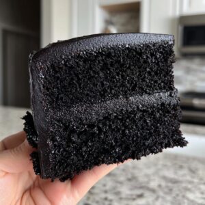 A hand holding a slice of moist black velvet halloween cake with rich chocolate frosting.