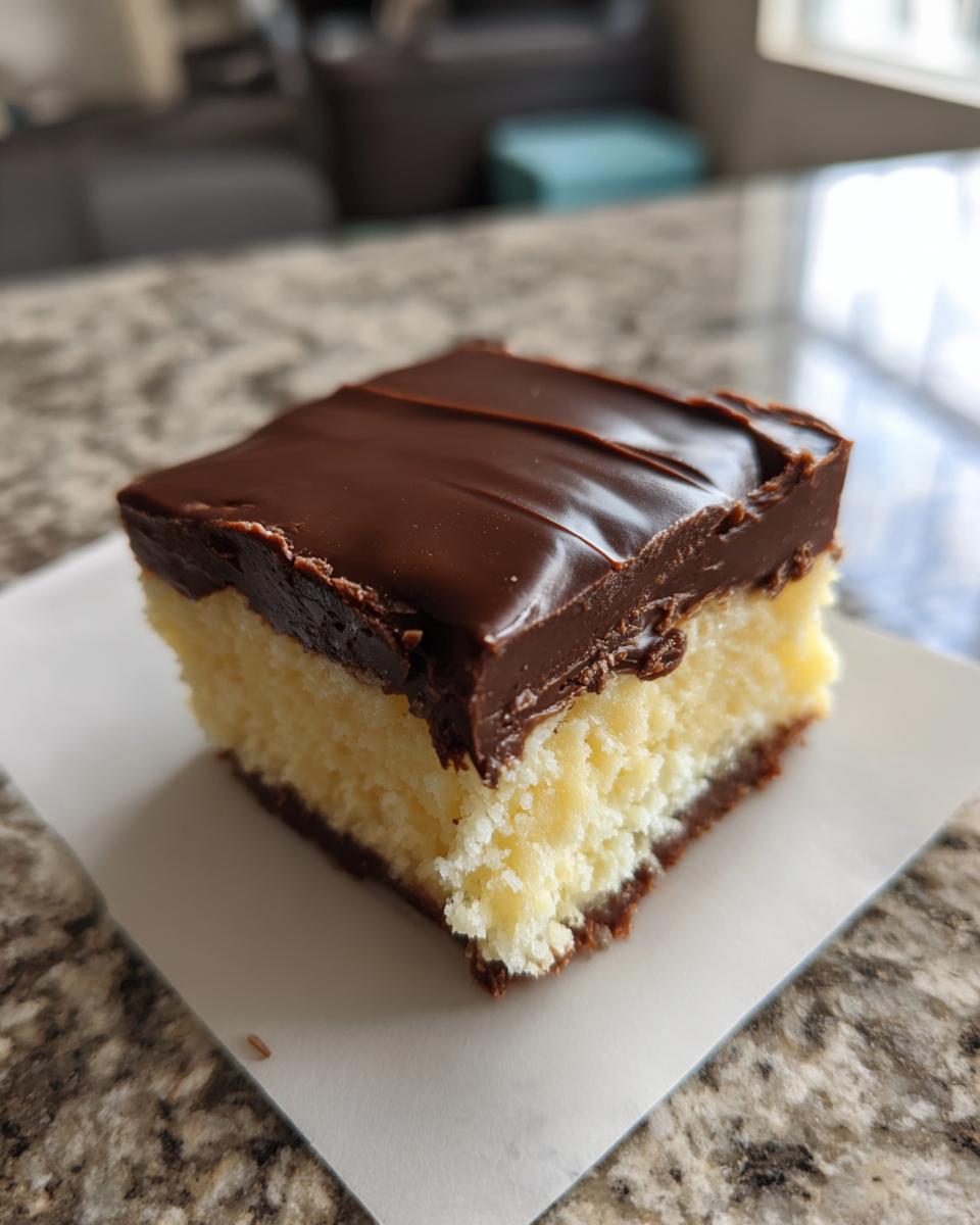 A close-up of a square slice of Boston Cream Pie Fudge, showing the creamy yellow filling and rich chocolate ganache topping.