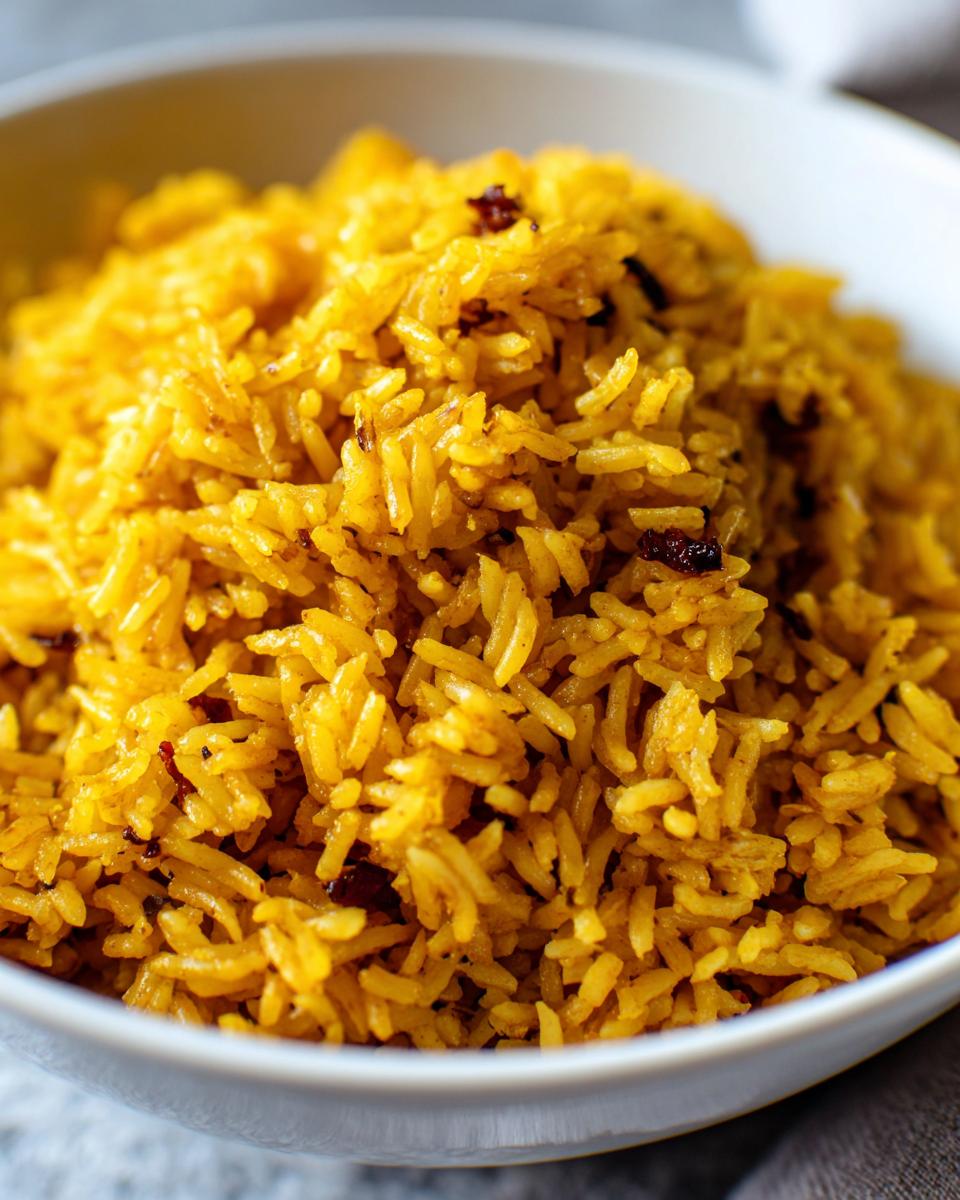 Close-up of fluffy, vibrant yellow turmeric rice served in a white bowl, showing individual grains.
