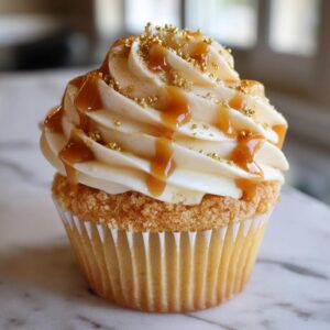 A close-up of a delicious Butterbeer cupcake topped with swirl frosting, caramel drizzle, and gold sprinkles.