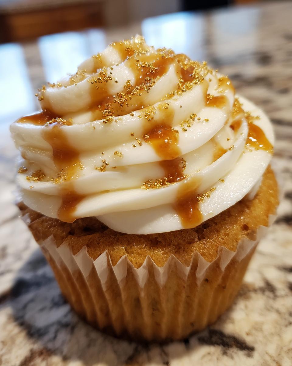 A close-up of a delicious Butterbeer cupcake topped with white frosting, caramel drizzle, and gold edible glitter.