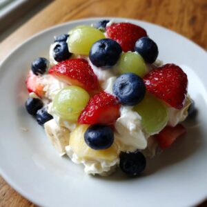 A vibrant serving of cheesecake fruit salad topped with strawberries, blueberries, green grapes, and creamy topping.