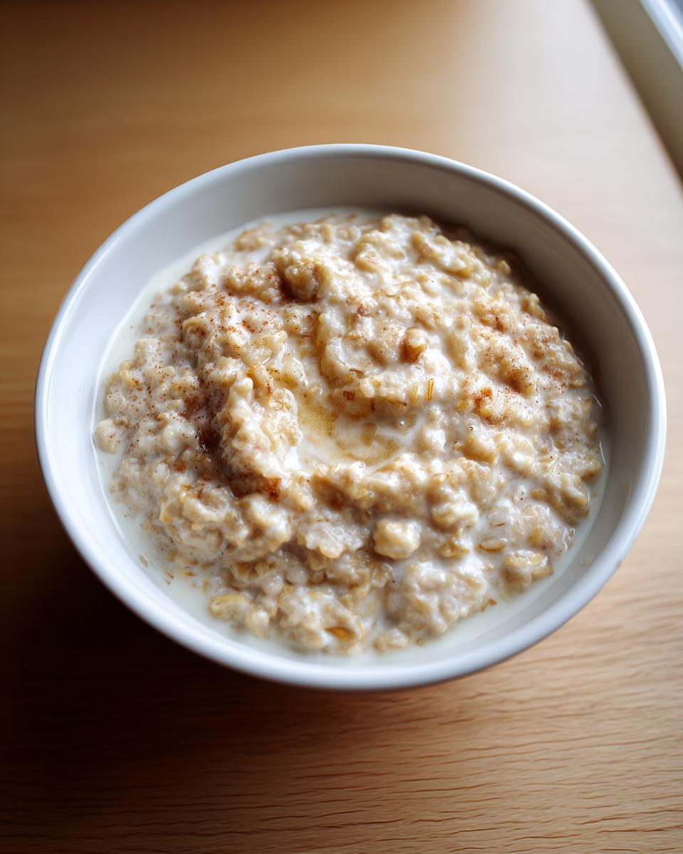 A white bowl filled with creamy banana oatmeal, topped with milk and a sprinkle of cinnamon.