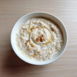 Overhead view of a white bowl filled with creamy banana oatmeal topped with a swirl of honey and nuts.