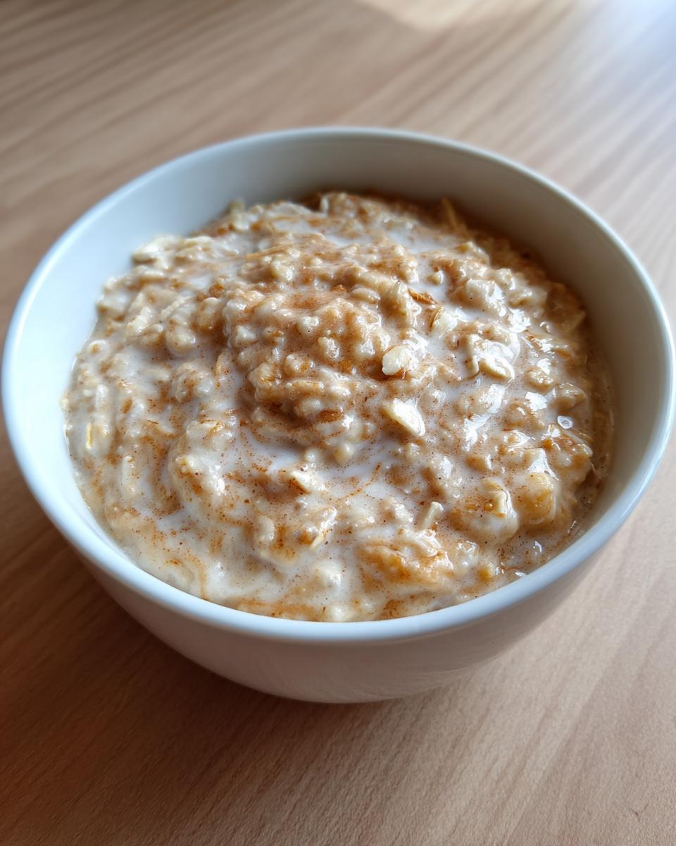A white bowl filled with creamy banana oatmeal topped with a swirl of milk and a dusting of cinnamon.
