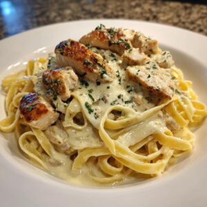 Close-up of creamy chicken alfredo pasta topped with sliced, seared chicken breast and parsley.