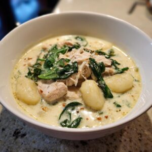 Close-up of creamy chicken gnocchi soup with spinach and shredded chicken in a white bowl.