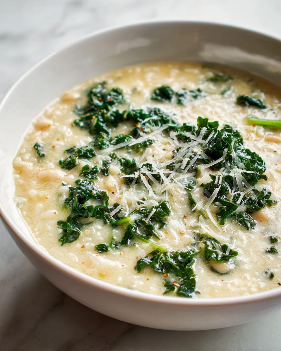 A close-up of creamy Tuscan white bean soup topped with wilted kale and grated Parmesan cheese.