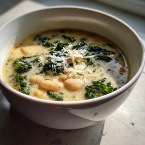 A close-up of creamy Tuscan white bean soup featuring cannellini beans, dark green kale, and topped with shredded Parmesan cheese.