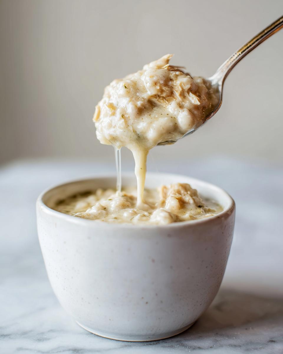 A spoonful of creamy white chicken chili being lifted from a small white bowl, showing dripping sauce.