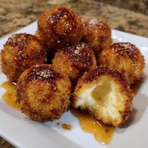 Close-up of crispy fried goat cheese balls drizzled with honey, one is broken open showing the melted interior.