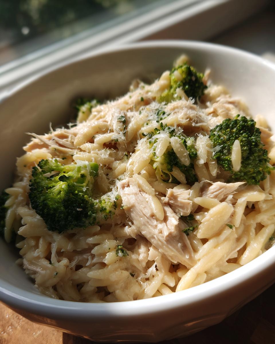 A bowl of creamy Crockpot Chicken Alfredo Orzo with tender chicken pieces and vibrant broccoli florets, topped with grated Parmesan.