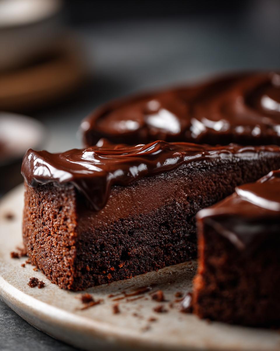 A close-up of a moist slice of easy chocolate cake topped with glossy, dark chocolate ganache.