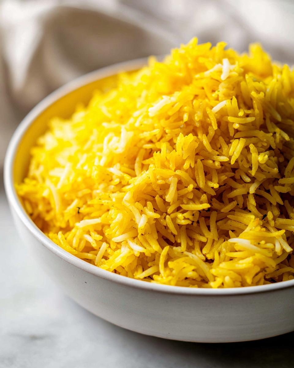 Close-up of vibrant yellow turmeric rice served in a white ceramic bowl.