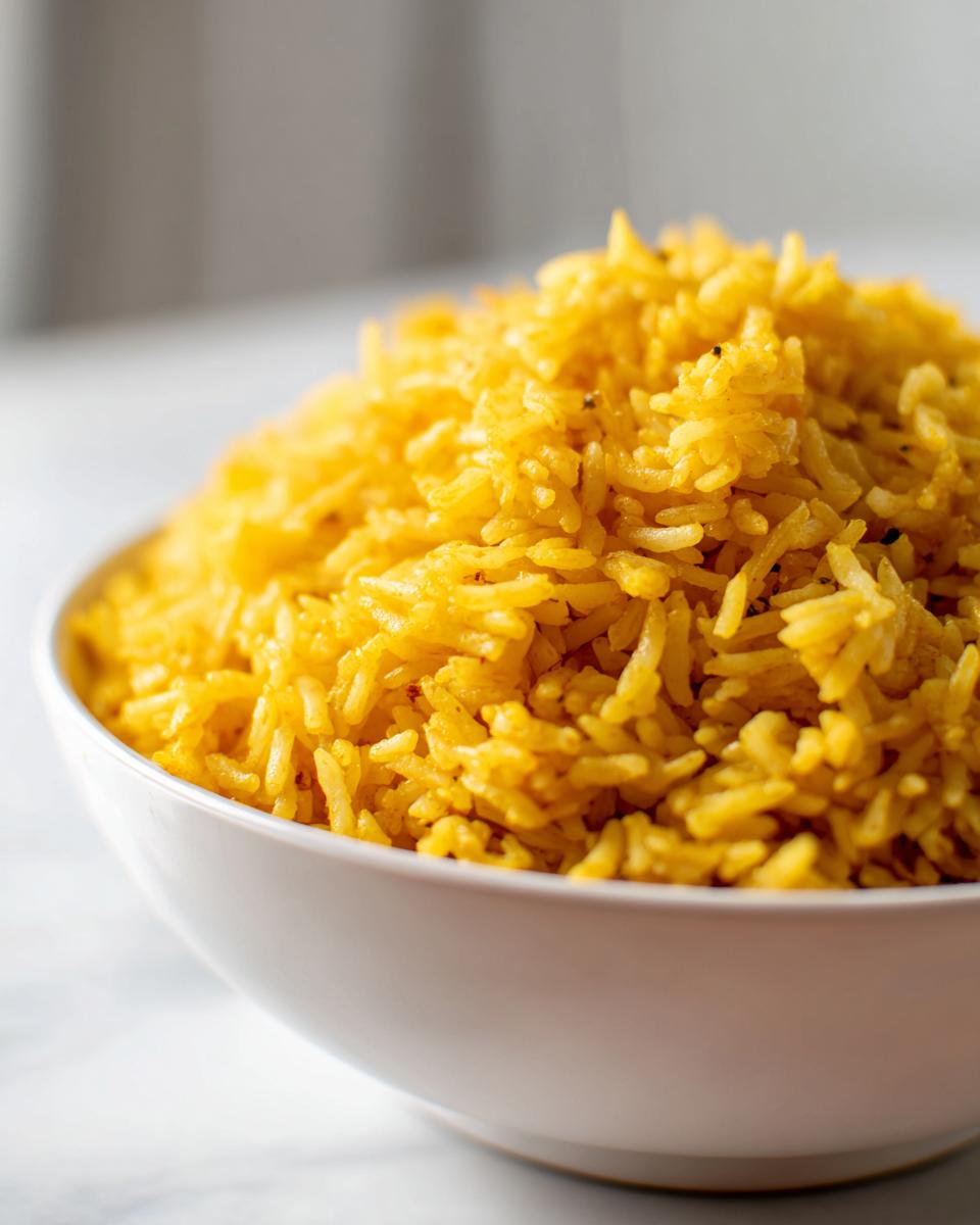 Close-up of fluffy, bright yellow turmeric rice served in a white bowl.