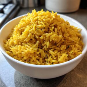 Close-up of a white bowl filled with vibrant, fluffy turmeric rice speckled with green herbs.