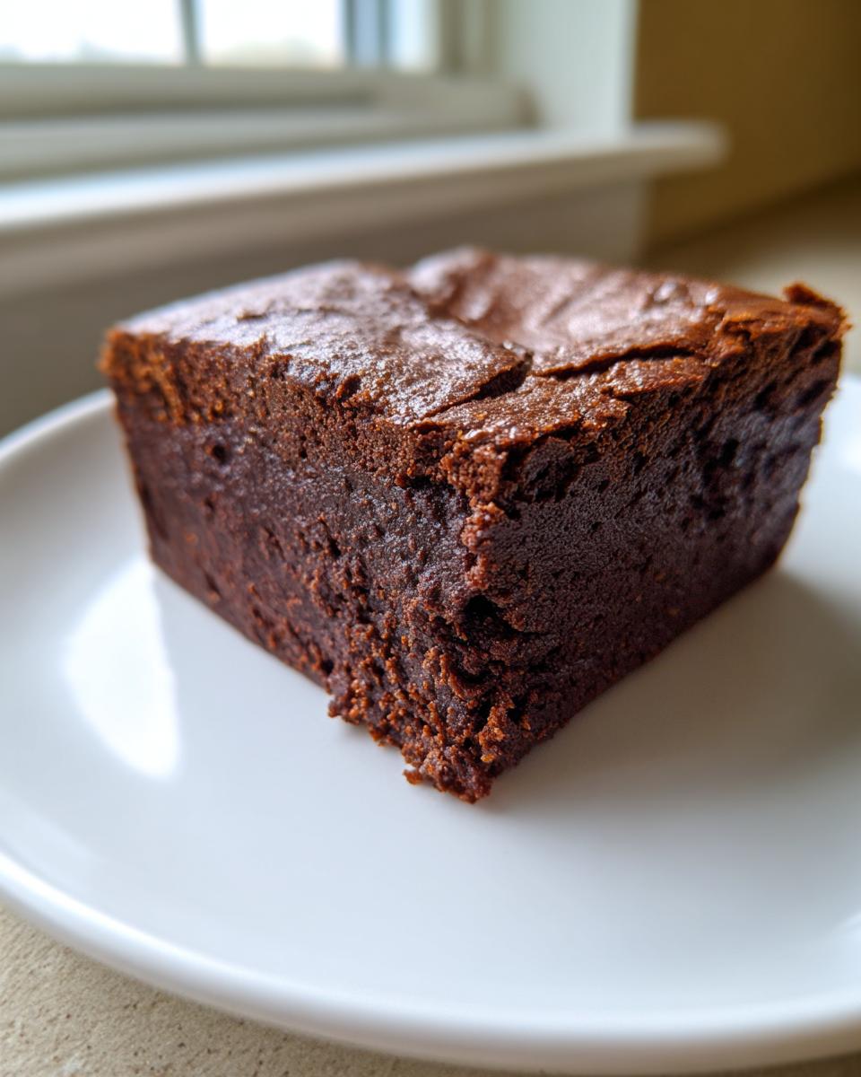 A close-up of a thick, fudgy square of sweet potato brownies with a shiny, cracked top.