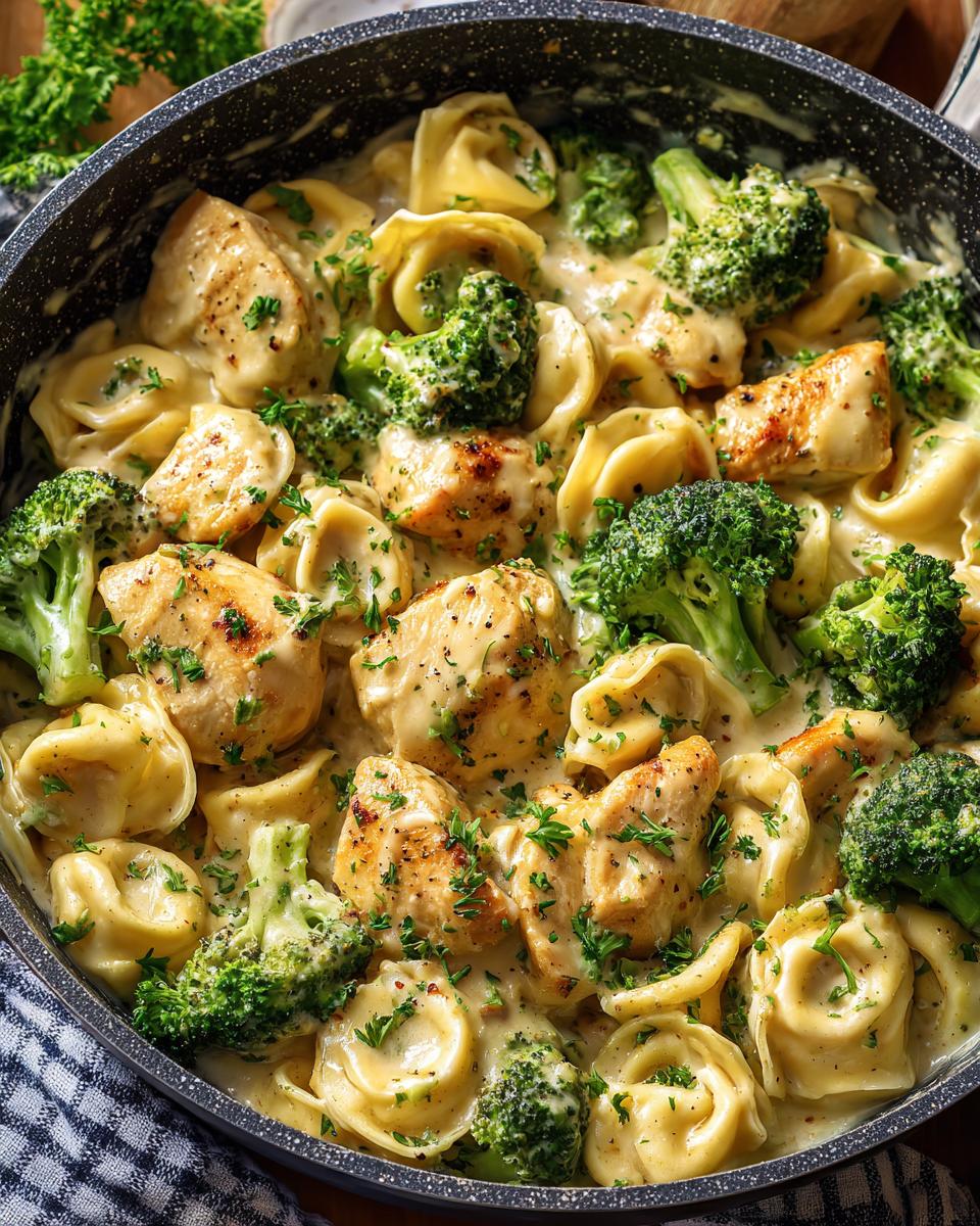 A close-up overhead view of Garlic Parmesan Chicken Broccoli Tortellini in a skillet, garnished with parsley.