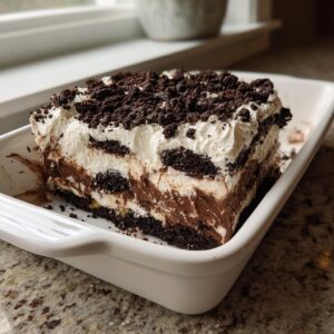 A thick, layered slice of rich chocolate dirt cake with cream and cookie crumbs in a white dish.