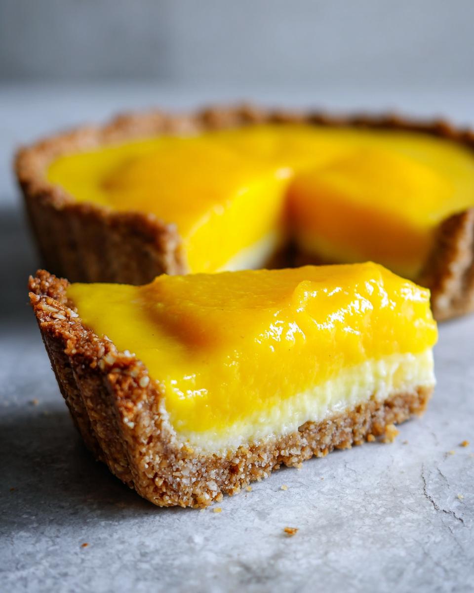 A close-up of a slice of mango curd tart, showcasing its vibrant yellow filling and nutty crust.