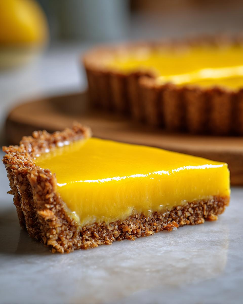 Close-up of a slice of mango curd tart, showcasing its vibrant yellow filling and textured nutty crust.