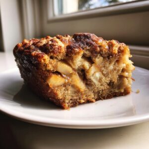 Close-up of a moist slice of apple cake showing chunks of baked apple and a crunchy brown sugar topping.