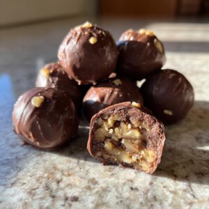 A pile of chocolate-covered Pecan Pie Brownie Bombs, with one cut in half to reveal the rich, nutty interior.