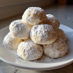 A mound of freshly baked russian tea cakes heavily dusted with powdered sugar, stacked on a white plate.