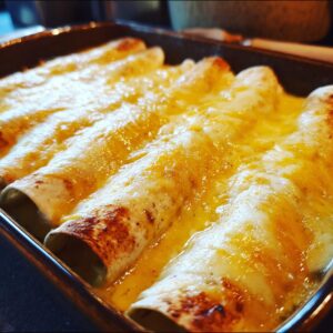 Close-up of baked queso chicken enchiladas in a casserole dish, covered in melted cheese.