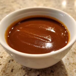 Close-up of rich, dark brown turkey gravy with a glossy surface in a small white bowl.