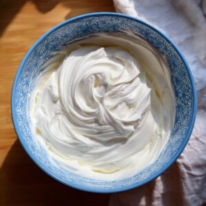 Close-up overhead view of thick, glossy white royal icing recipe mixture swirled in a blue patterned bowl.