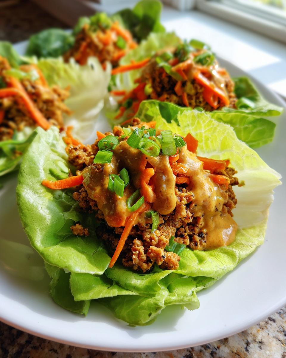 Four servings of delicious thai chicken lettuce wraps filled with seasoned ground chicken, shredded carrots, and topped with peanut sauce and green onions.