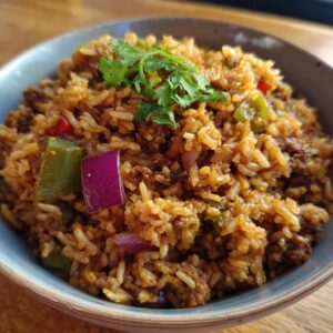 A close-up of a bowl filled with flavorful Vegan Dirty Rice, featuring rice, plant-based crumbles, bell peppers, and red onion, garnished with cilantro.