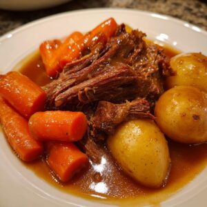 Close-up of tender shredded pot roast served with whole cooked carrots and small potatoes in rich brown gravy.