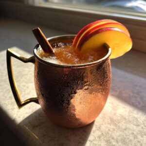 A frosty copper mug filled with an apple cider Moscow mule, garnished with apple slices and a cinnamon stick.