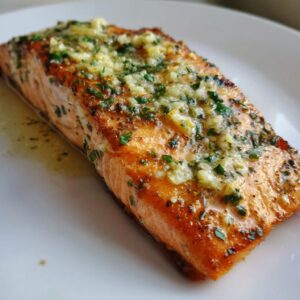 Close-up of a perfectly cooked baked salmon recipe fillet topped with melted garlic butter and fresh parsley.
