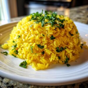 A mound of vibrant yellow mediterranean rice, garnished generously with fresh chopped parsley, served on a white plate.