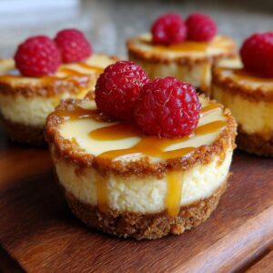 A close-up of a delicious mini cheesecake topped with caramel drizzle and fresh raspberries.
