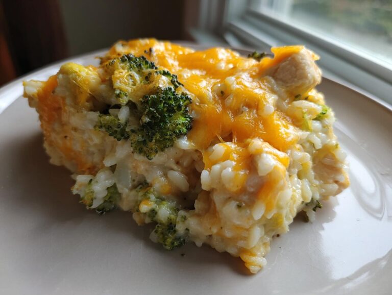 A close-up serving of creamy chicken broccoli rice casserole topped with melted cheddar cheese.