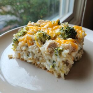 A square serving of creamy chicken broccoli rice casserole topped with melted cheddar cheese.