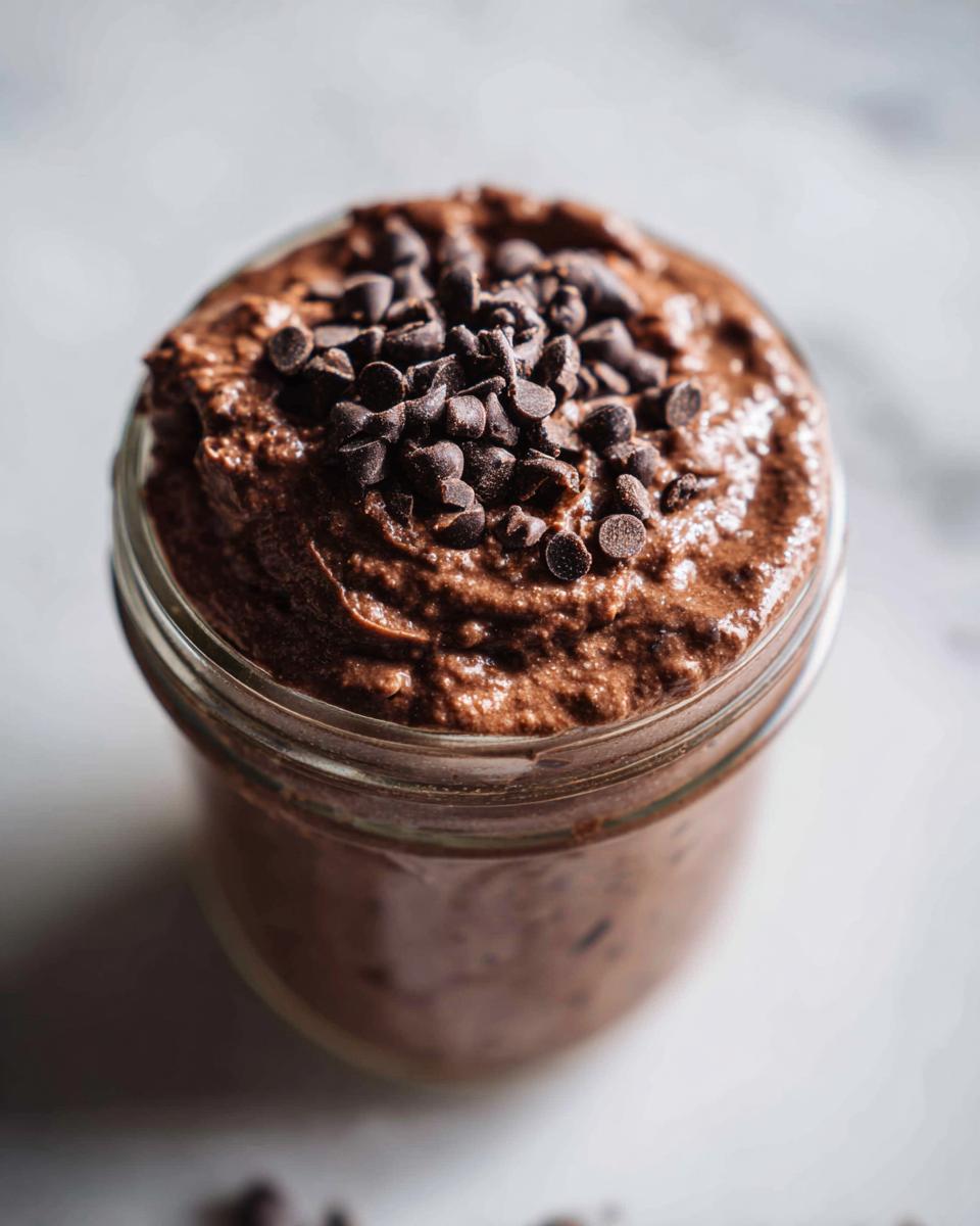 Close-up of rich chocolate overnight oats in a glass jar topped generously with mini chocolate chips.