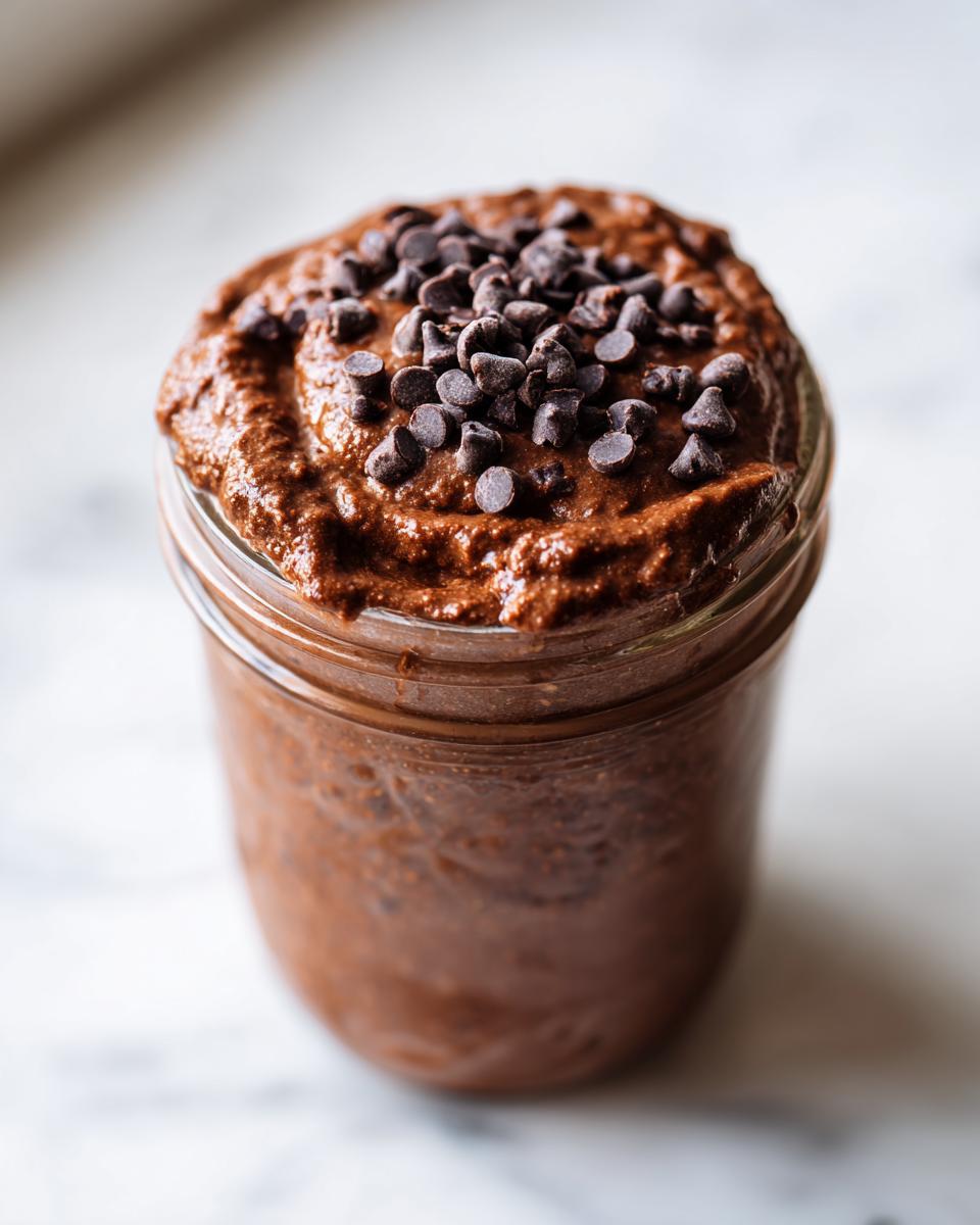 Close-up of rich chocolate overnight oats in a glass jar, topped generously with mini chocolate chips.