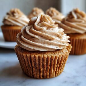 A close-up of a moist banana cupcakes topped with a swirl of cinnamon-dusted frosting.