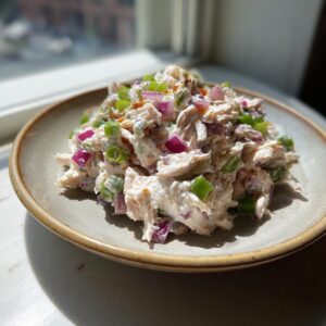 A mound of creamy cottage cheese chicken salad mixed with diced red onion and green onions on a light brown plate.