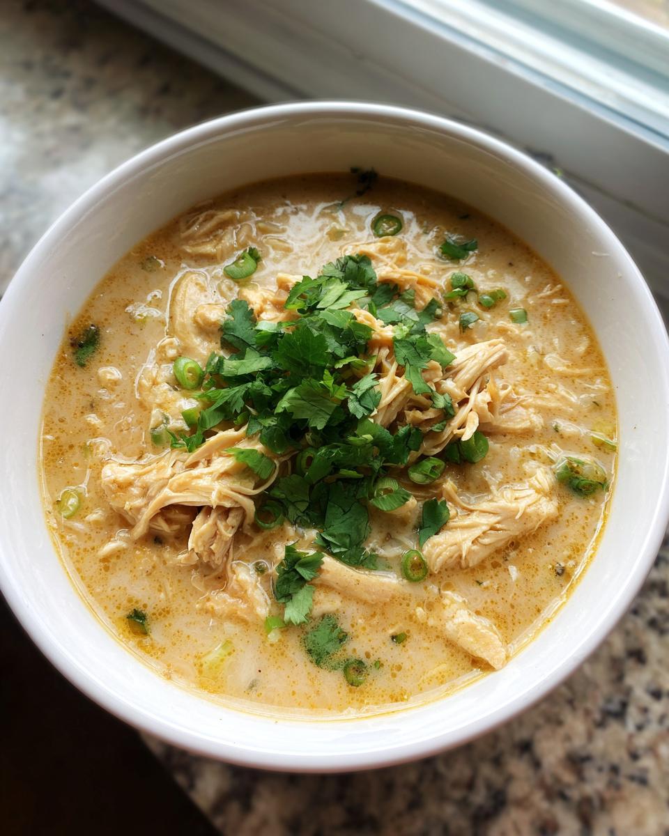 Overhead view of a white bowl filled with creamy keto white chicken chili, topped with shredded chicken and fresh cilantro.