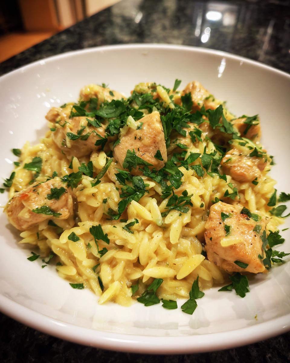 A close-up of creamy lemon chicken orzo topped generously with fresh chopped parsley in a white bowl.